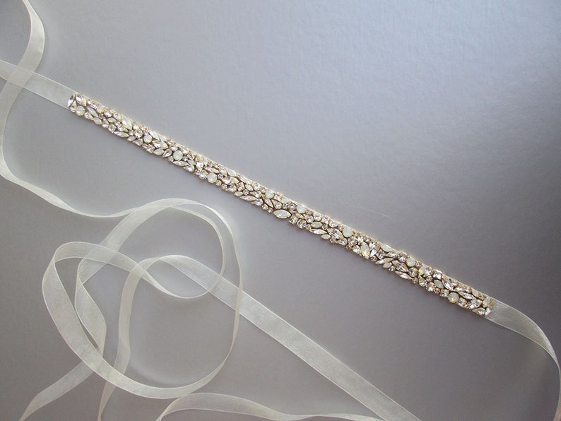 May include: A delicate ivory satin ribbon with a gold-toned embellishment of clear and iridescent rhinestones. The ribbon is approximately 1.5 inches wide and is perfect for adding a touch of sparkle to any outfit.