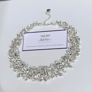 May include: A silver bridal hairpiece with a delicate design of crystal leaves. The hairpiece is made by "Salvya Design" and is described as "Fine Hair Jewelry and Accessories".