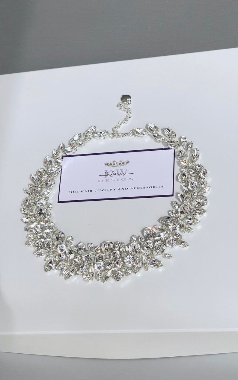 May include: A silver bridal hairpiece with a delicate design of crystal leaves. The hairpiece is made by "Salvya Design" and is described as "Fine Hair Jewelry and Accessories".