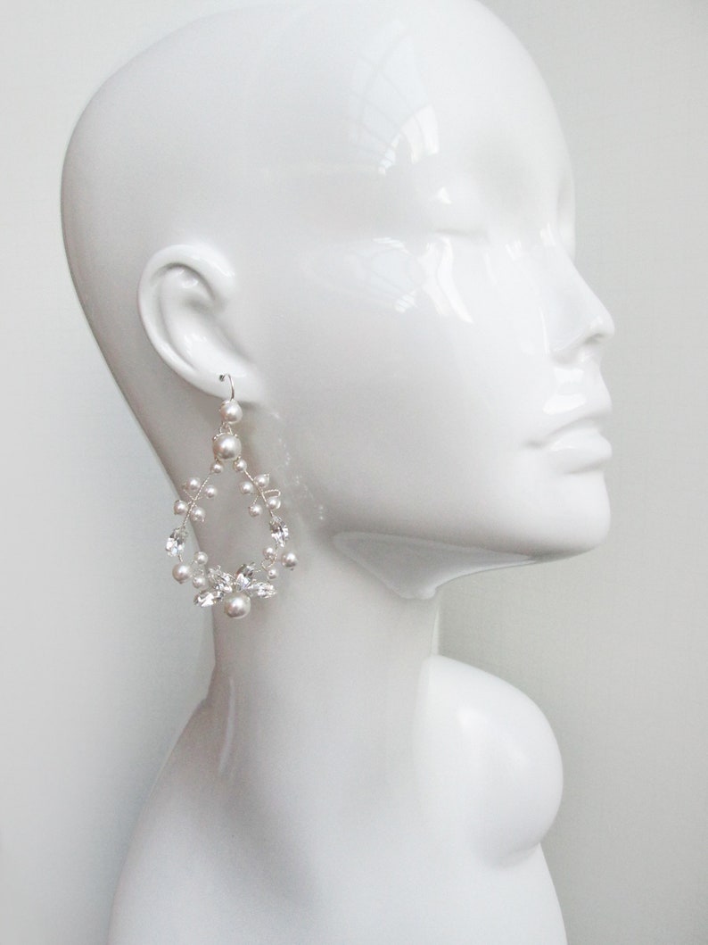May include: Silver teardrop shaped earrings with white pearls and clear crystals.