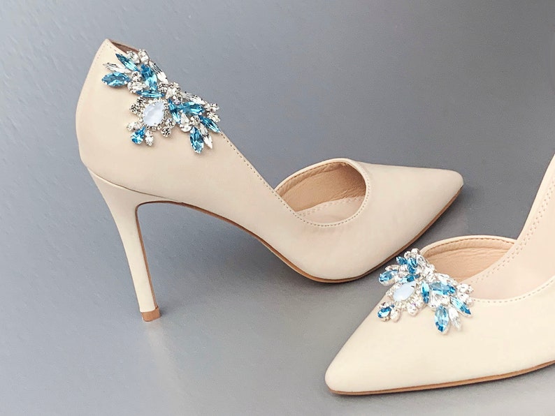 May include: A pair of beige high-heeled shoes with blue crystal embellishments on the toes.