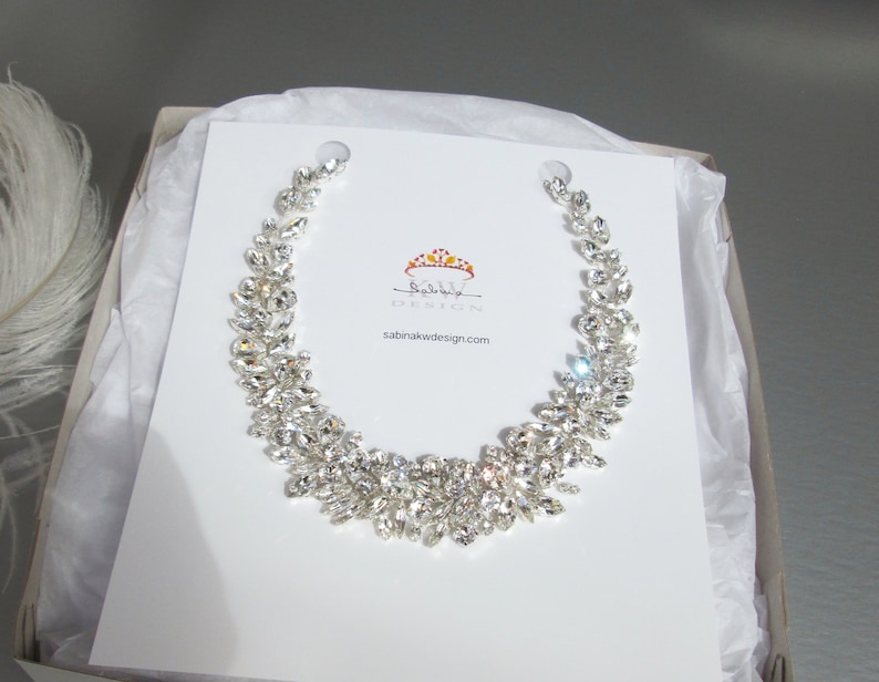 May include: A silver crystal necklace with a crown logo and the text "Sabina K Wedding Design" and the website "sabinakwdesign.com".