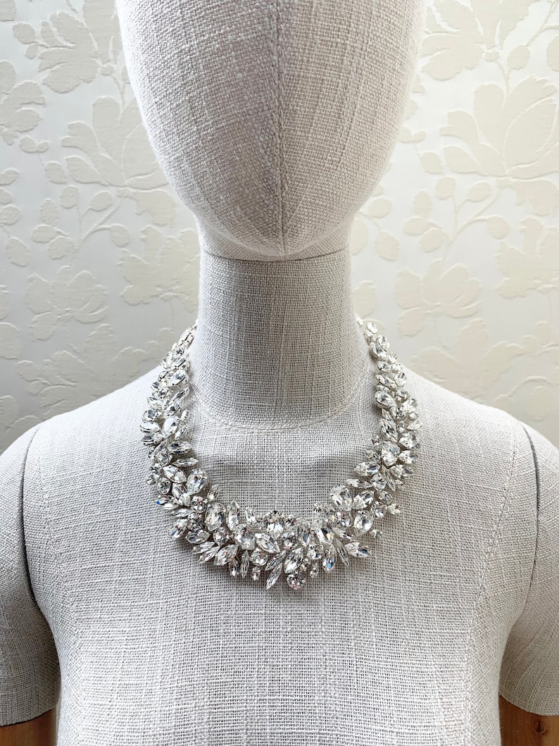 May include: A silver statement necklace with large, clear crystal stones arranged in a floral pattern.