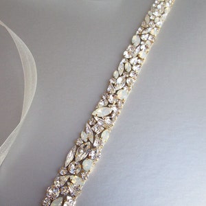 May include: A white satin ribbon embellished with a row of clear and iridescent rhinestones. The rhinestones are set in gold metal.