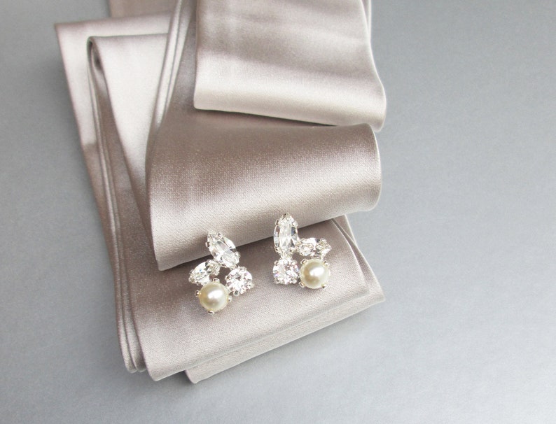 May include: A pair of silver earrings with a cluster of clear rhinestones and a single pearl on each earring.