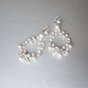 May include: A pair of silver earrings with a delicate design featuring white pearls and clear crystals. The earrings are shaped like a teardrop and dangle from the earlobe.