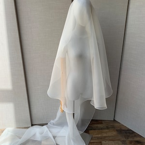 Pu&ograve; includere: Un velo da sposa in tulle bianco a strato singolo con bordo smerlato. Il velo &egrave; drappeggiato su un manichino e cade sul pavimento.