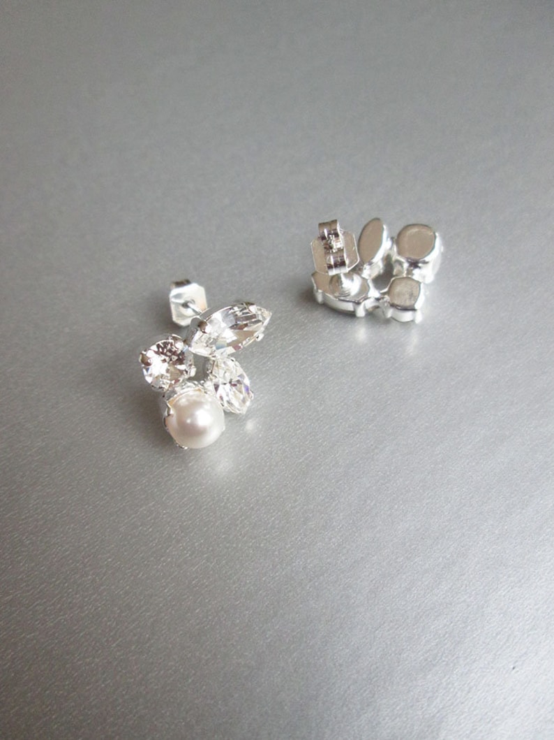 May include: A pair of silver earrings with clear crystal and pearl accents. The earrings have a post back fastening.