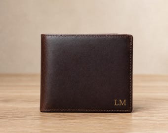 Op de afbeelding: Een donkerbruine leren bifold portemonnee met zichtbare stiksels langs de randen en de in reliëf aangebrachte hoofdletters LM in de rechterbenedenhoek. De portemonnee heeft een gladde, matte afwerking en een rechthoekige vorm met afgeronde hoeken.