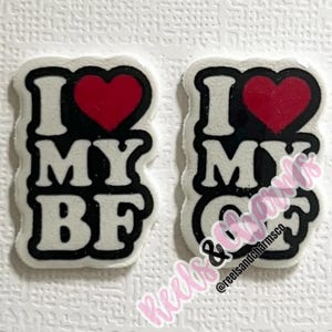 May include: Two white rectangular stickers with black borders and black text. The left sticker reads I LOVE MY BF with a red heart. The right sticker reads I LOVE MY GF with a red heart. Both stickers feature a bold, blocky font style.
