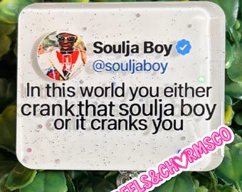 Op de afbeelding: Een rechthoekige witte badge met glitteraccenten met een ronde profielfoto van Soulja Boy, de tekst Soulja Boy @souljaboy met een blauw geverifieerd vinkje en het citaat In this world you either crank that soulja boy or it cranks you.