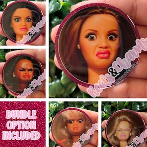 May include: A collection of round, glitter-rimmed pins featuring doll faces with exaggerated expressions. The pins showcase various doll faces with surprised or displeased expressions. The text "BUNDLE OPTION INCLUDED" is visible on a pink glitter background.