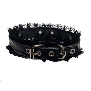 May include: Black choker collar with a lace trim. The collar is made of black leather and features a silver buckle and a metal ring. The brand name "DAUNTING CLAWS" is visible in the bottom left corner.