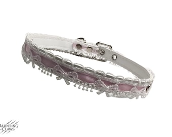 May include: White leather pet collar with a pink satin centre and silver lace trim. The collar has a silver buckle and D-ring. The Daunting Claws logo is in the bottom left corner.