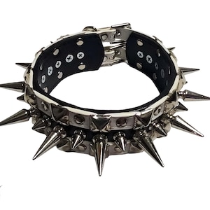 Puede incluir: Un collar tachonado blanco y negro con púas plateadas. El collar tiene un exterior blanco, un interior negro y herrajes de metal plateado. Las púas están espaciadas uniformemente alrededor del exterior del collar. El collar está diseñado para una mascota.