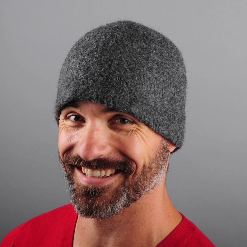 May include: A man wearing a gray wool beanie with a red shirt. He is smiling and looking at the camera.