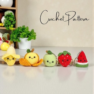 Può includere: Una collezione di cinque portachiavi a forma di frutta all'uncinetto: una banana, un'arancia, una mela, una fragola e un'anguria. Ogni frutto ha una faccia sorridente ed è realizzato con filato colorato. Il testo "Crochet Pattern" è scritto in corsivo.