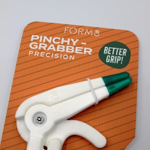May include: A white and green precision grabber tool with the text "PINCHY-GRABBER PRECISION" on an orange background. The tool has a white handle and green tips, with the words "BETTER GRIP!" in a green circle.