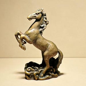 以下が含まれることがあります： ブロンズ色の立ち上がった馬の像。馬は、なびくたてがみと尾を含む詳細な特徴で彫刻されています。渦巻き模様の装飾的な台座の上に立っています。この像は装飾品です。