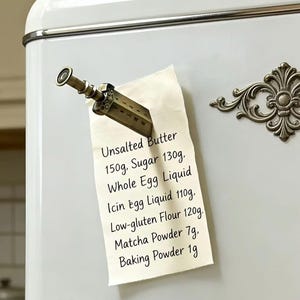 May include: A vintage-style refrigerator with a decorative metal clip holding a recipe card. The card lists baking ingredients: unsalted butter, sugar, whole egg liquid, icing egg liquid, low-gluten flour, matcha powder, and baking powder.