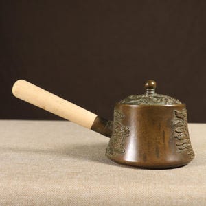 Puede incluir: Cucharón antiguo de bronce con mango de madera. El cucharón presenta intrincados grabados en relieve de dragones y flores en el cuerpo y la tapa. El mango está sujeto con un accesorio de latón. Para servir o verter líquidos.