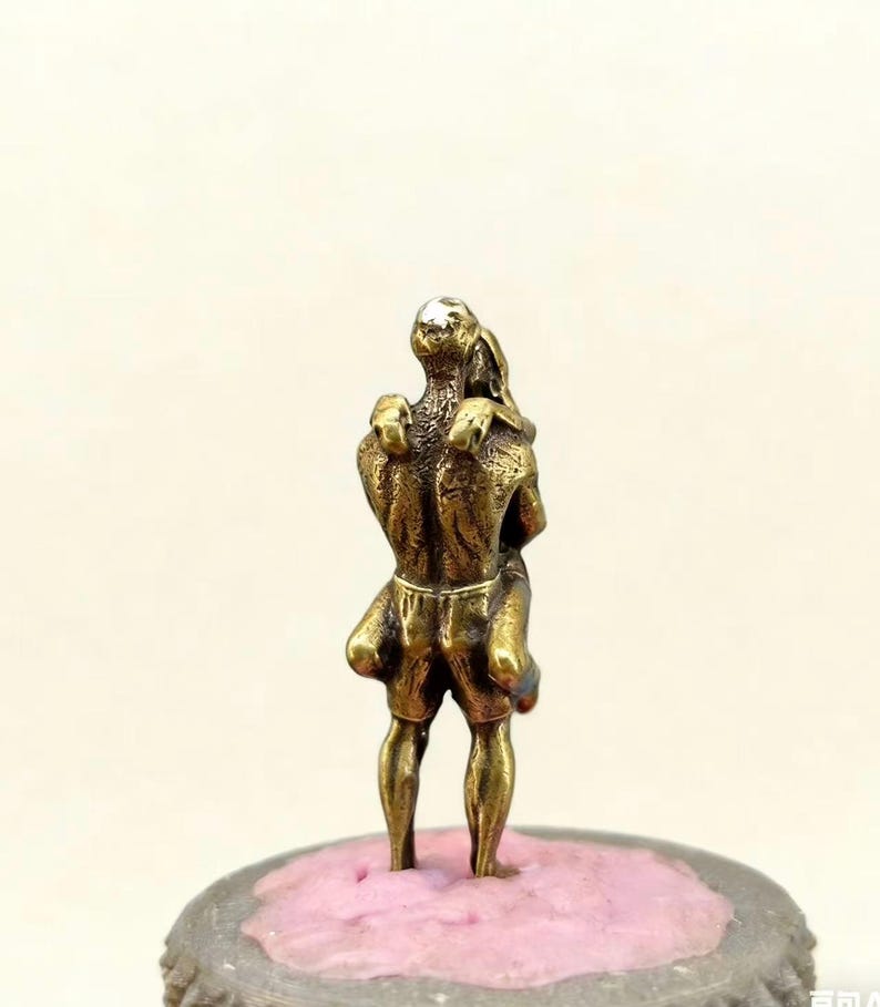 Puede incluir: Peque&ntilde;a escultura de color bronce que representa dos figuras abraz&aacute;ndose. Las figuras est&aacute;n estilizadas con detalles, de pie sobre una base rosa y gris. La escultura tiene una est&eacute;tica vintage.