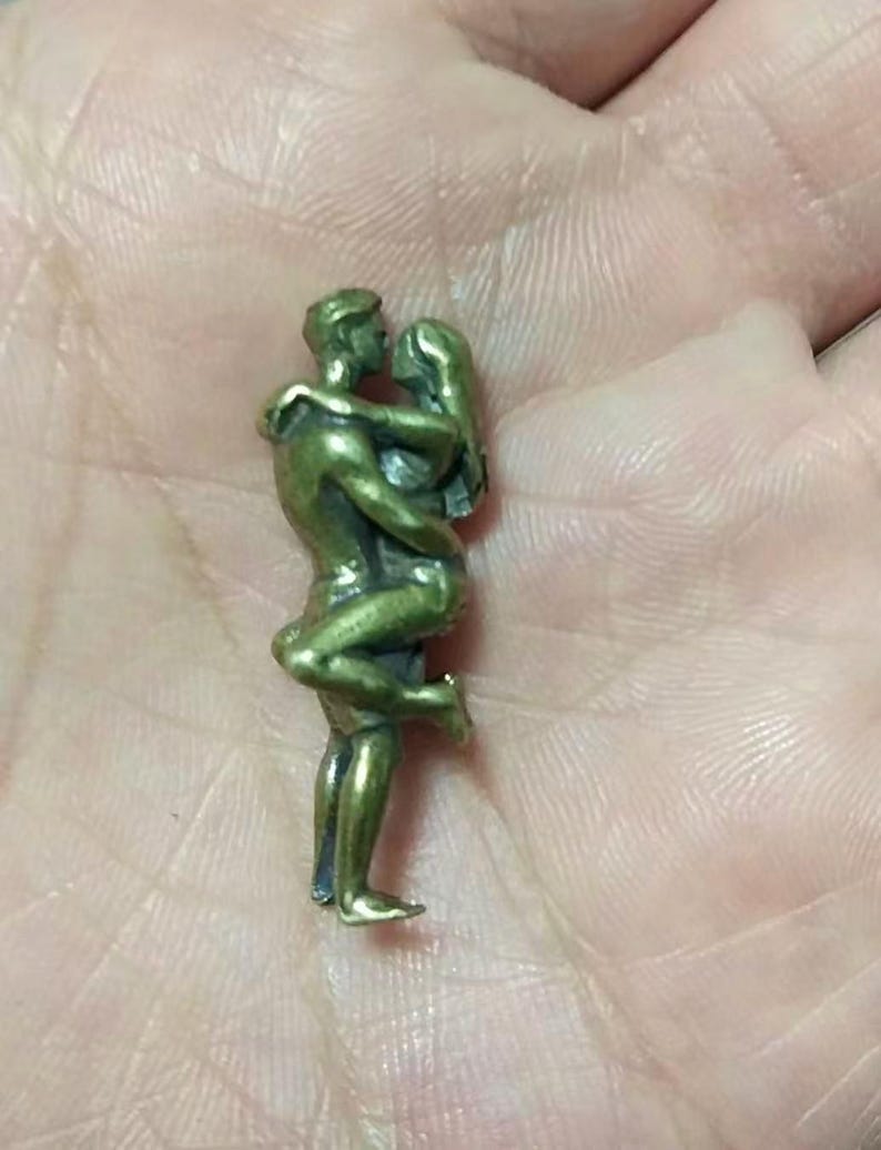 Puede incluir: Peque&ntilde;a escultura de color bronce que representa a una pareja abraz&aacute;ndose. El hombre sostiene a la mujer, que se inclina hacia atr&aacute;s. La escultura es detallada, mostrando los rasgos y la ropa de las figuras. Es probable que sea un objeto decorativo.