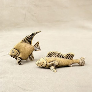 May include: Two bronze-colored fish sculptures. One fish has a tall, curved dorsal fin, while the other lies flat. Both have detailed fins and scales, and are likely decorative items.