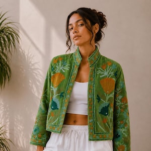 May include: A green jacket featuring a mandarin collar and long sleeves, decorated with embroidered floral patterns in orange, teal, and light blue. The jacket is worn over a white cropped tank top and white drawstring trousers.