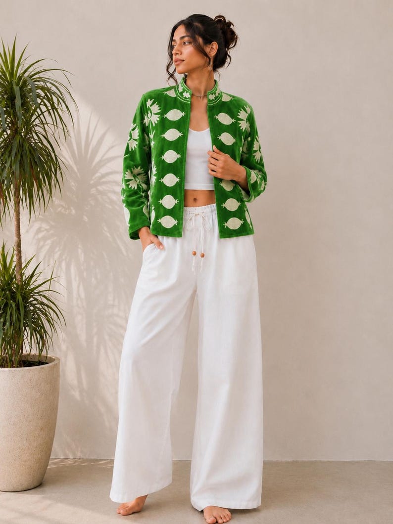 May include: A vibrant green jacket featuring a white floral and geometric pattern, worn over a white cropped tank top and loose-fitting white wide-leg trousers with a drawstring waist and wooden bead accents at the ends of the cord.
