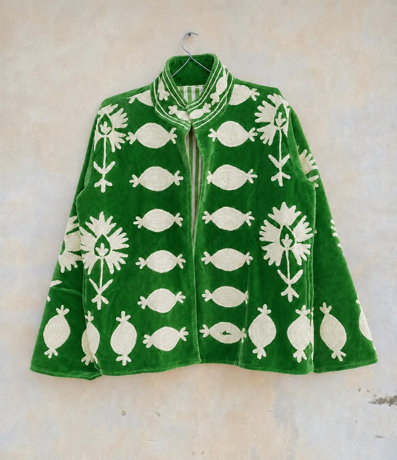 May include: A vibrant green jacket featuring an open front, a high collar, and long sleeves. The garment is decorated with cream-colored embroidered floral and oval-shaped motifs arranged in a repeating pattern across the entire surface.