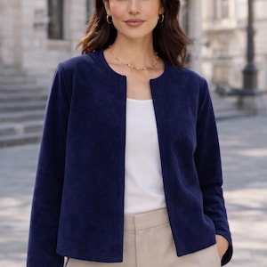 Op de afbeelding: Marineblauwe jas met een ronde halslijn en lange mouwen. De jas wordt gedragen over een witte top en gecombineerd met beige broeken. De outfit is geschikt voor diverse gelegenheden.