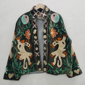Peut inclure: Veste en velours vert foncé avec des détails brodés colorés. La veste présente un col mandarin, une doublure rayée et est ornée de motifs floraux, animaux et yin-yang dans des tons orange, turquoise et rose.