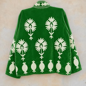 May include: A vibrant green velvet jacket featuring cream-colored floral embroidery. The back displays a repeating pattern of large stylized flowers above a row of smaller rounded motifs. The collar also features matching cream floral embroidery.