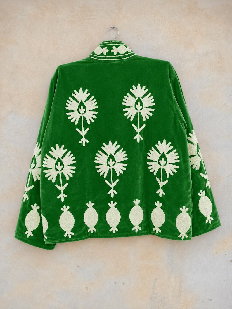 May include: A vibrant green velvet jacket featuring cream-colored floral embroidery. The back displays a repeating pattern of large stylized flowers above a row of smaller rounded motifs. The collar also features matching cream floral embroidery.