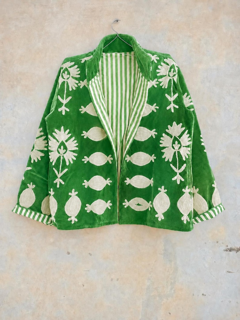 May include: A vibrant green jacket featuring cream-colored floral and abstract embroidery. The garment has long sleeves with striped cuffs, a stand-up collar, and an interior lining that displays a vertical cream and green striped pattern.