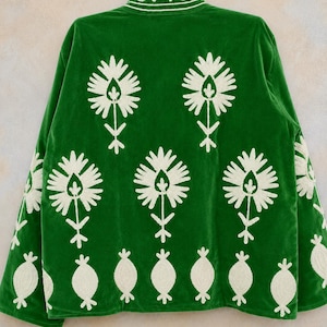May include: A vibrant green jacket featuring white embroidered floral motifs across the back and sleeves. The design includes large stylized flower patterns and a row of smaller oval shapes along the bottom hem, with matching embroidery on the collar.
