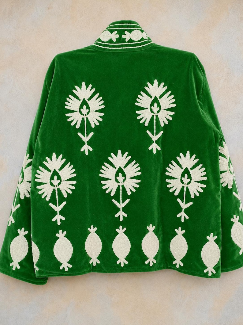 May include: A vibrant green jacket featuring white embroidered floral motifs across the back and sleeves. The design includes large stylized flower patterns and a row of smaller oval shapes along the bottom hem, with matching embroidery on the collar.