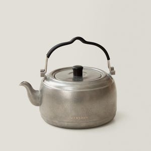 May include: A silver-toned metal kettle with a black handle and lid. The kettle has a spout and a rounded body. The word "WENSHUO" is printed on the front of the kettle.