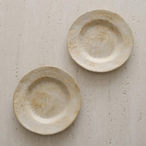 May include: Two off-white ceramic plates with a textured surface. The plates have a slightly irregular shape and a warm, neutral color palette, suitable for serving food. The plates are set against a light background.