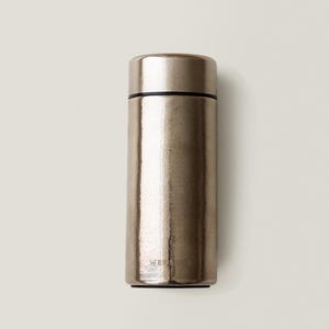 May include: A metallic silver insulated water bottle with a black band near the top. The bottle has a cylindrical shape and a screw-on lid. The text "WE S CO" is printed on the bottom of the bottle.