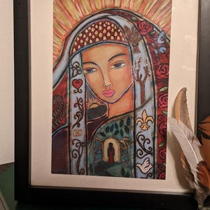 May include: A framed painting of a woman with a colorful, intricate design around her. The woman has a soft, gentle expression and is surrounded by symbols of nature and spirituality. The painting is set against a white background.