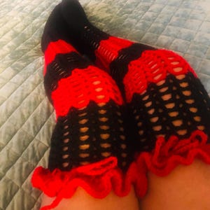 May include: A pair of black and red crochet thigh-high socks. The socks feature alternating bands of black and red, with a scalloped red trim at the top. The open weave design is visible.