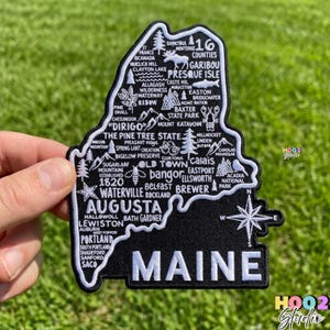 May include: A set of three ceramic mugs with a speckled, cream-colored glaze. Each mug features a different hand-painted design: a blue and green leaf, a yellow flower, and a red berry. The mugs have a simple, rounded shape.