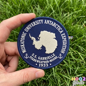 May include: A round, navy blue patch with white embroidered text and a map of Antarctica. The text reads "Miskatonic University Antarctica Expedition" and "S.S. Gabrielle Starkweather-Moore 1933". Two anchors are also embroidered on the patch.