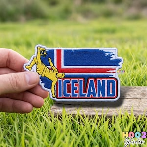 May include: Embroidered patch featuring the flag of Iceland with a soccer player in yellow. The patch has a blue background with red and white stripes, and the word "ICELAND" in white with a blue border. The patch is held against a background of green grass.
