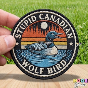 May include: Embroidered patch featuring a loon on a lake, with the text "STUPID CANADIAN WOLF BIRD" in a circular design. The patch has a black border, a sunset background, and a full moon. The loon is blue and white.