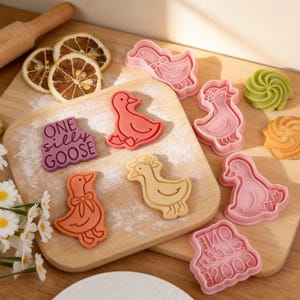 A 4-piece goose-themed cookie cutter set for baking. Features a text stamp saying "ONE silly GOOSE" alongside designs of a goose wearing a bonnet, a goose with a bow tie, and a swimming duck. Shown with colorful dough impressions and dried lemon slices on a wooden board.