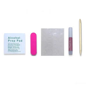 May include: A nail kit with an alcohol prep pad, a pink nail file, a sheet of adhesive nail tabs, a tube of nail glue, and a wooden cuticle pusher. The alcohol prep pad has the text "Alcohol Prep Pad" and other text in multiple languages.
