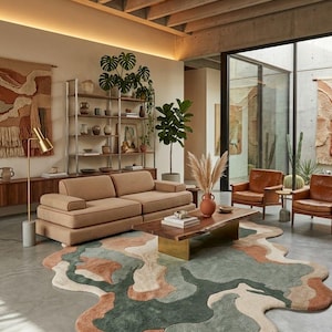 May include: An irregular, organic-shaped area rug featuring a multi-colored abstract pattern in shades of sage green, terracotta, cream, and beige. The rug is placed on a concrete floor in a living room setting with a sofa, coffee table, and chairs.